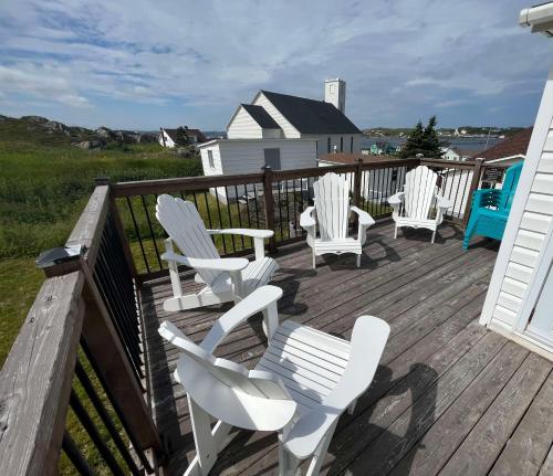 a deck with white chairs and tables and a house at Stockley's Saltbox in Twillingate