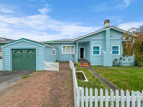 uma casa azul com uma cerca branca em frente em Green Getaway- Unique, 4 bedroom Bungalow Papakura em Auckland