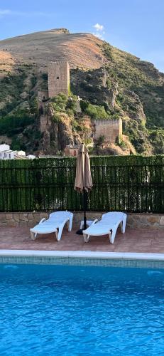 a pool with two chairs and an umbrella and a castle at Casa Angel in Cazorla