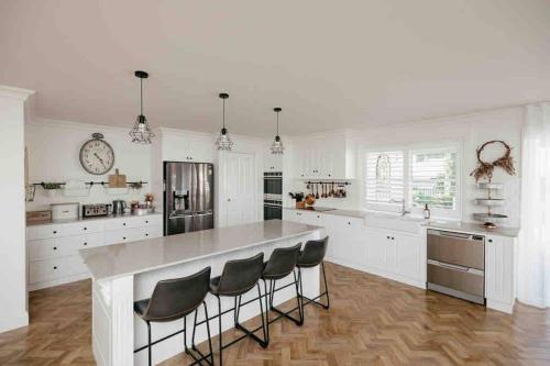 a white kitchen with a large island with bar stools at Cosy Country Cottage in Alstonville