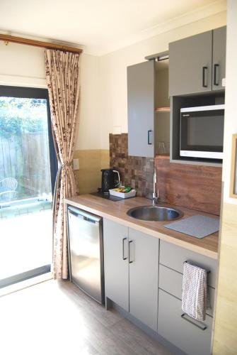 a kitchen with white cabinets and a sink and a window at Energy Motor Lodge Papamoa in Tauranga