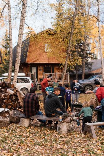 a group of people sitting around a fire in front of a house at Alaska Cozy Cabins in Wasilla