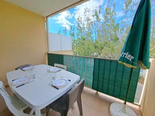 une table blanche avec des chaises et un parasol vert sur un balcon dans l'établissement Appartement 2 pièces accès direct plage avec parking privé - FR-1-326-823, à Marseillan