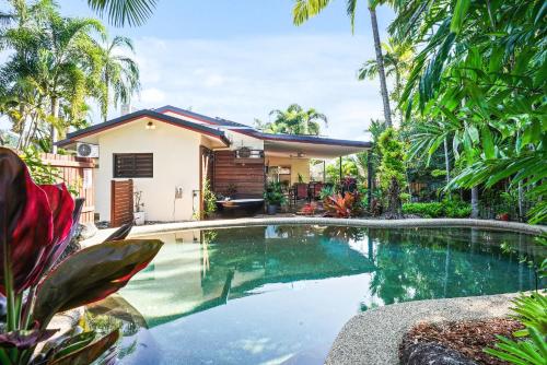 a swimming pool in front of a house with palm trees at Sudbury Shores Beach House in Kewarra Beach
