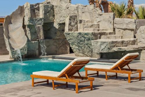 two lounge chairs next to a pool with a waterfall at Pecan Valley Oasis - Lux Pool, Sauna and Theater in Hurricane