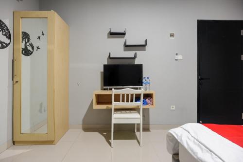 - une chambre avec un bureau, une télévision et un lit dans l'établissement RedDoorz near Jakarta International Velodrome, à Jakarta