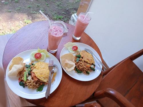 zwei Teller Essen auf einem Holztisch mit Getränken in der Unterkunft Jepun Homestay Lemukih in Singaraja