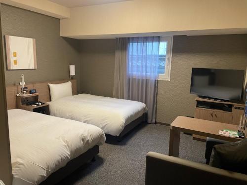 a hotel room with two beds and a flat screen tv at Hotel Route-Inn Sakurai Ekimae in Sakurai