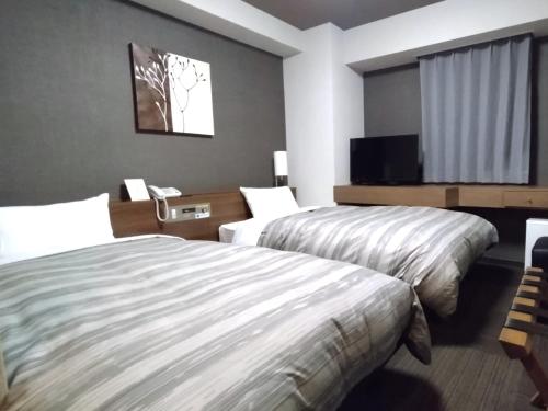 a hotel room with two beds and a flat screen tv at Hotel Route-Inn Hitachitaga in Hitachi