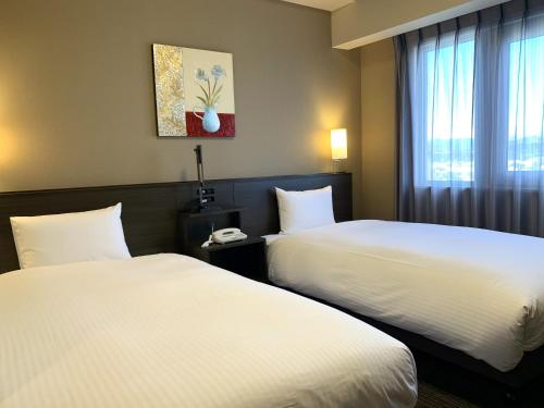 a hotel room with two beds and a window at Hotel Route-Inn Isesaki Inter in Isesaki