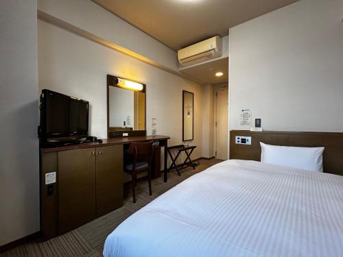 丸亀市にあるホテルルートイン丸亀のベッド、デスク、テレビが備わるホテルルームです。