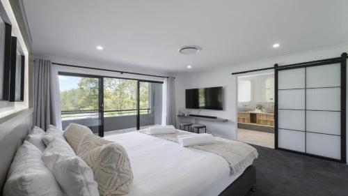 a white bedroom with a large bed and a large window at Tallowwood in Pokolbin
