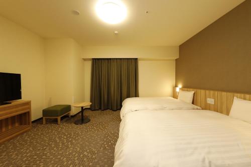 a hotel room with two beds and a flat screen tv at Dormy Inn Maebashi in Maebashi