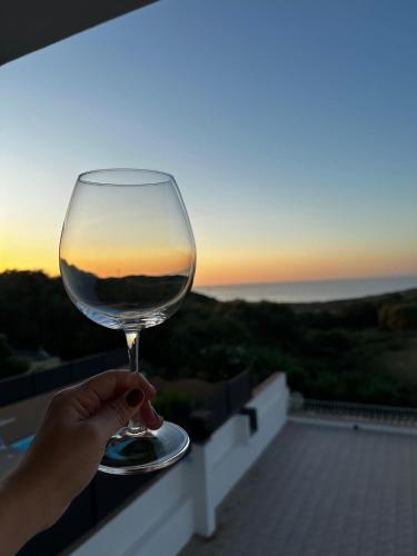 a person holding a wine glass with the sunset in the background at Costa Rossa View Sunset in Cascabraga