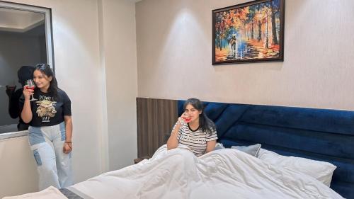 two women are taking pictures of a girl sitting on a bed at Raksha Suites & Banquet Greater Noida in Greater Noida
