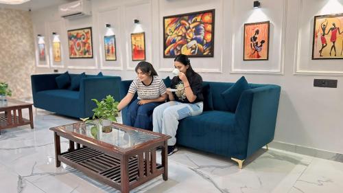 two women sitting on a couch in a living room at Raksha Suites & Banquet Greater Noida in Greater Noida
