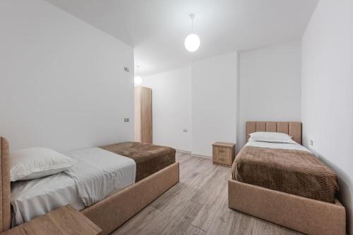 two beds in a bedroom with white walls and wooden floors at City Escape Apartment in Shkodër