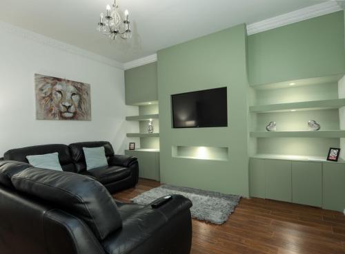 a living room with a black leather couch and a television at Sunderland Self Catering 2 - Violet Cottage Free Parking in Sunderland