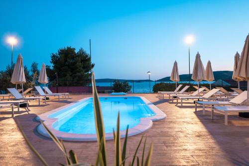 a swimming pool with lounge chairs and umbrellas at Apartments Medena in Trogir