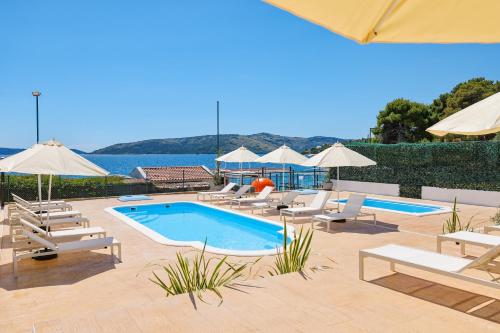 a pool with chairs and umbrellas next to the water at Apartments Medena in Trogir