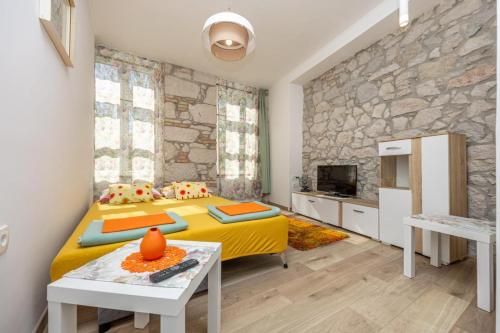 a bedroom with a yellow bed and a stone wall at Apartmani Leo centar in Crikvenica