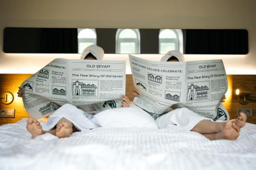 two people laying on a bed reading newspapers at Old Ijevan Boutique Hotel in Ijevan