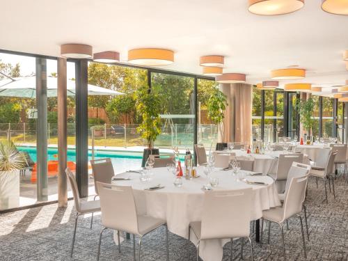 a dining room with white tables and chairs and a pool at Holiday Inn Toulouse Airport by IHG in Blagnac