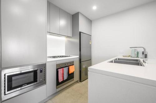 a white kitchen with a stove and a refrigerator at Olympic Park with View Parking near Train in Sydney