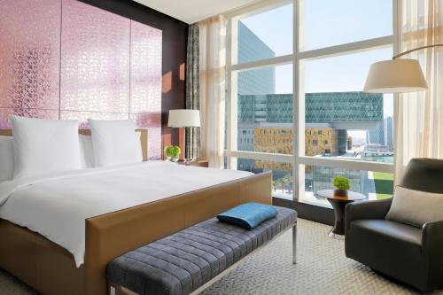 a bedroom with a bed and a chair and a large window at Rosewood Abu Dhabi in Abu Dhabi