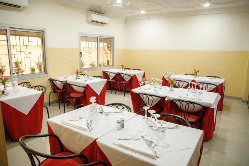 une salle à manger avec des tables blanches et des chaises rouges dans l'établissement Residence Diane, à Ouagadougou