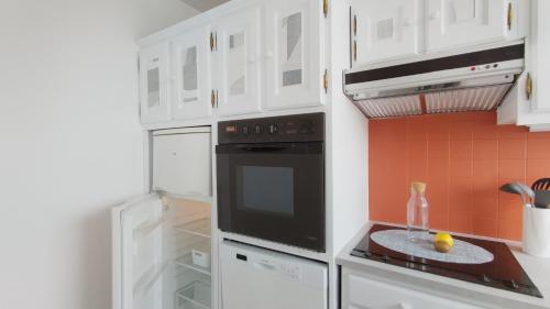 La cuisine est équipée de placards blancs et d'un four avec plaques de cuisson noires. dans l'établissement Studio Spacieux vue sur Paris et Tour Eiffel Proche Paris, à Fontenay-aux-Roses