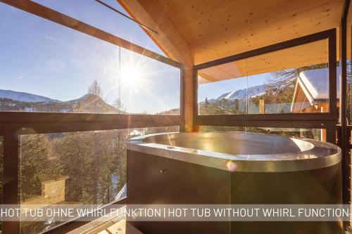 uma banheira de hidromassagem num quarto com uma grande janela em Naturchalets Turracher Höhe by ALPS RESORTS em Turracher Höhe