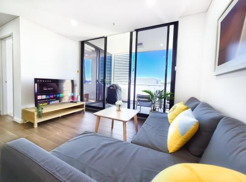 a living room with a couch and a tv at Relaxing 1BR w Pools & SPA, Gym in Olympic Park in Sydney