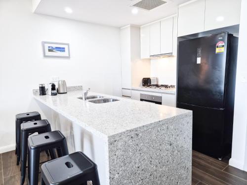 a kitchen with a black refrigerator and a counter with stools at Relaxing 1BR w Pools & SPA, Gym in Olympic Park in Sydney