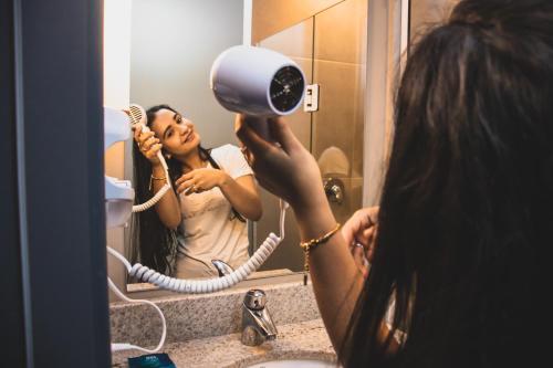a woman blow drying her hair in front of a mirror at ibis budget Navegantes Itajai in Itajaí