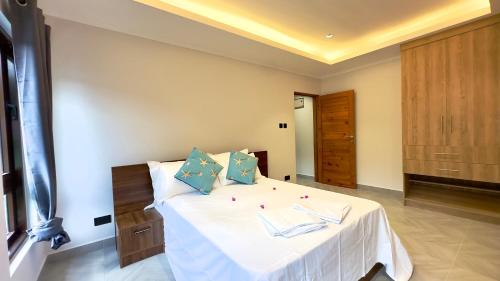 a bedroom with a bed with white sheets and blue pillows at Green Palm Self Catering in Anse aux Pins