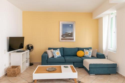 Una sala de estar con un sofá azul y un televisor. en Belle Epoque Tinos, en Tinos