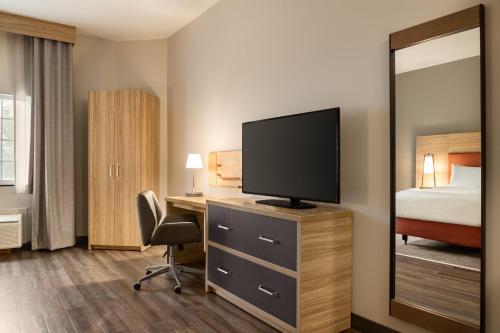 a hotel room with a desk with a television and a bed at Candlewood Suites Harrisburg I-81 Hershey Area by IHG in Harrisburg