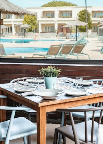 a wooden table with plates and chairs and a pool at Vincci Resort Costa Golf in Chiclana de la Frontera