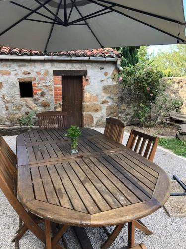 une table en bois avec des chaises et un parasol dans l'établissement Les Gouttes Hôtes - Maison de charme, à Essertines-en-Châtelneuf