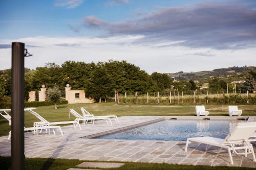 a pool with white lounge chairs next to a field at Villa Adelaide Relais & Wine in Calamandrana