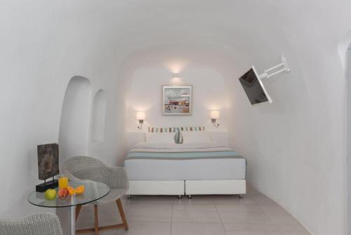 a white bedroom with a bed and a table at Caldera Premium Villas in Oia