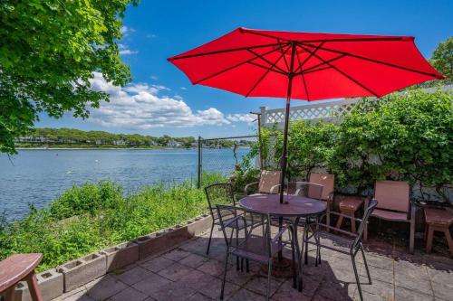 a table with a red umbrella next to the water at 39 Jefferson Shores Bourne - Vacation Bliss on Buttermilk Bay in Buzzards Bay