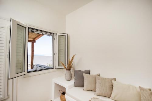 a white living room with a couch and two windows at Thea Suites Naxos in Agios Prokopios