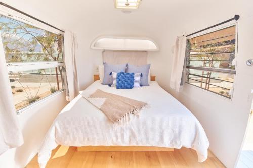 a small bedroom with a bed and two windows at Acres Landing in Desert Hot Springs