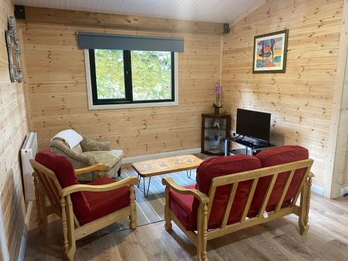 a living room with wooden walls and red chairs and a table at Rosies Cabin Maum in Galway