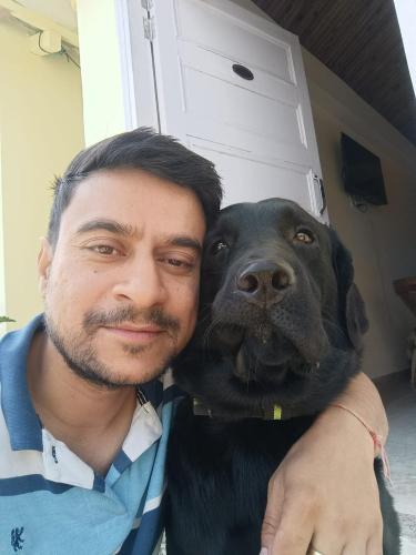 a man is hugging a black dog at THE HIDEAWAY Homestay Chail in Chail