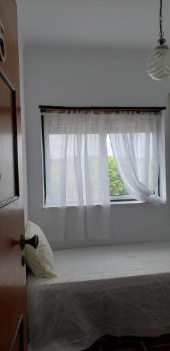 a bedroom with a window with white curtains at House Mariona in Caminha