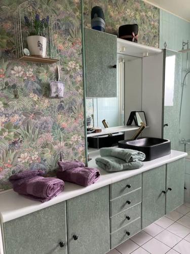 La salle de bains est pourvue d'un miroir et de serviettes pourpres sur un comptoir. dans l'établissement Le Refuge Du Bien Être, à Ruminghem