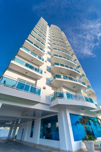 a tall white building with a palm tree in front of it at Elegante Aqua Marine Apartamento Juan Dolio in Juan Dolio